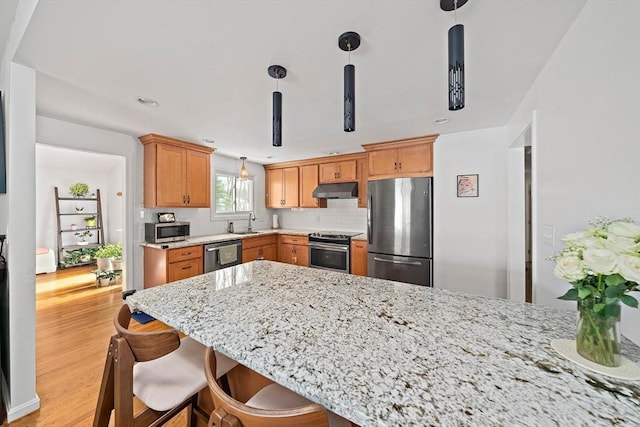 kitchen with a peninsula, appliances with stainless steel finishes, decorative light fixtures, and under cabinet range hood