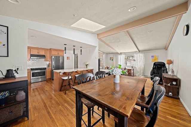 dining area with light wood-style floors, vaulted ceiling with skylight, and baseboards