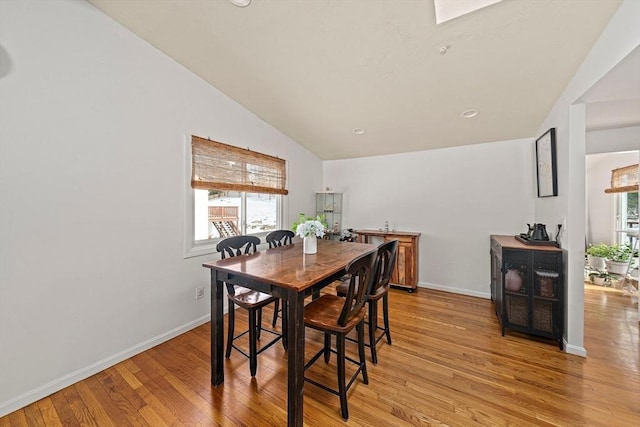 dining area featuring light wood finished floors, baseboards, and vaulted ceiling