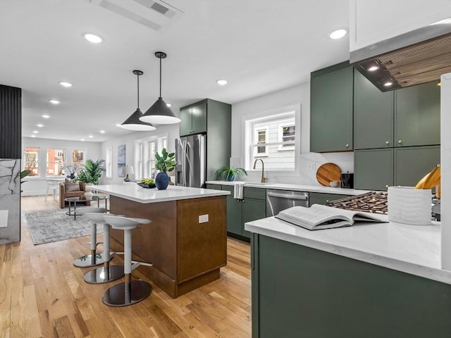 kitchen with a kitchen island, pendant lighting, stainless steel appliances, and green cabinetry