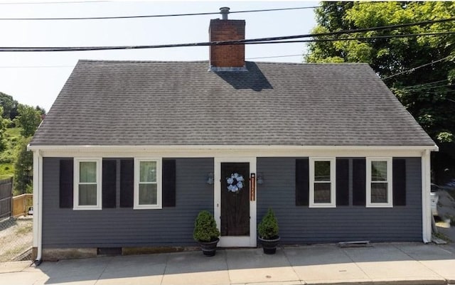 new england style home featuring a patio, a chimney, and roof with shingles