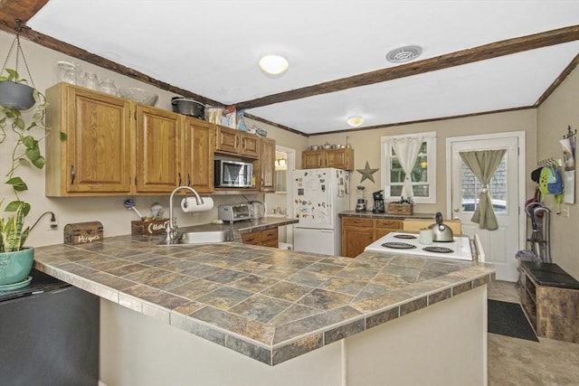 kitchen with a peninsula, freestanding refrigerator, a sink, crown molding, and stainless steel microwave