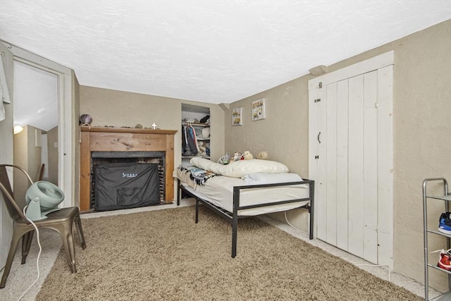 carpeted bedroom featuring a fireplace with flush hearth, a textured ceiling, and a textured wall