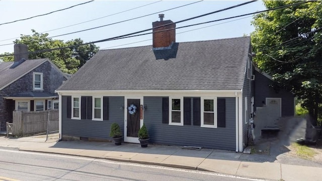 cape cod-style house featuring fence, roof with shingles, and a chimney