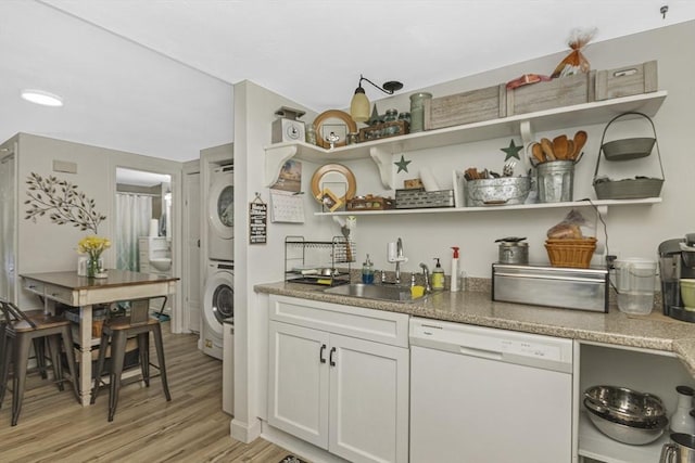 kitchen featuring dishwasher, open shelves, stacked washer / drying machine, and a sink