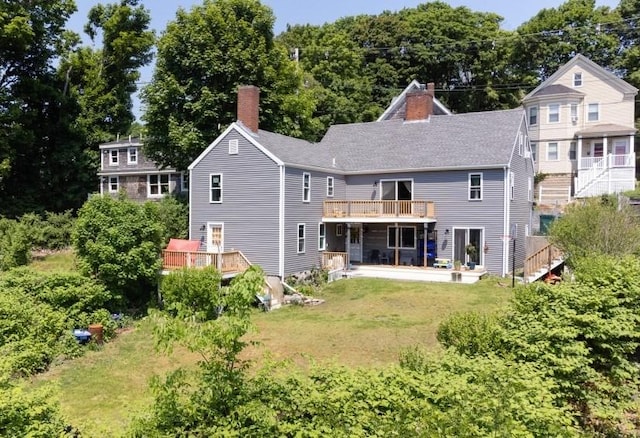 rear view of property featuring a wooden deck, a lawn, roof with shingles, and a chimney