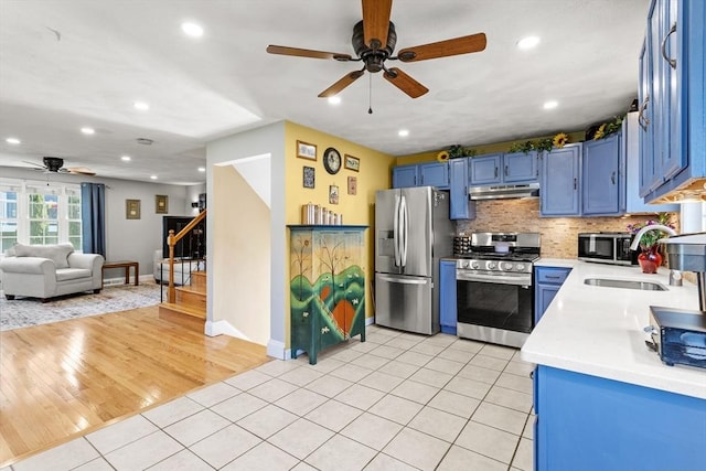 kitchen with light countertops, under cabinet range hood, stainless steel appliances, a ceiling fan, and blue cabinetry