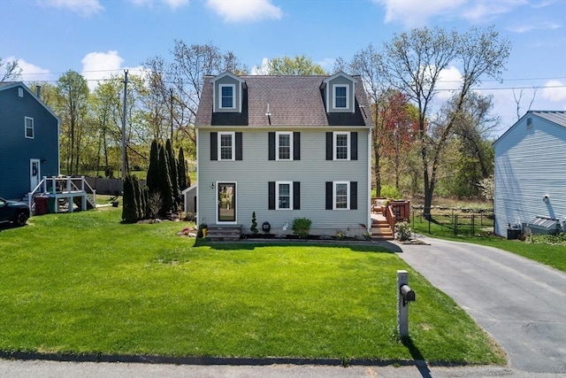 colonial-style house featuring fence, roof with shingles, driveway, and a front lawn