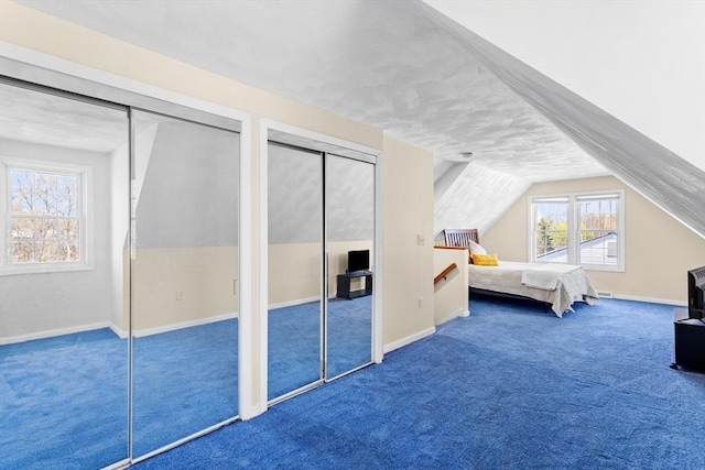bedroom featuring two closets, carpet flooring, baseboards, and lofted ceiling