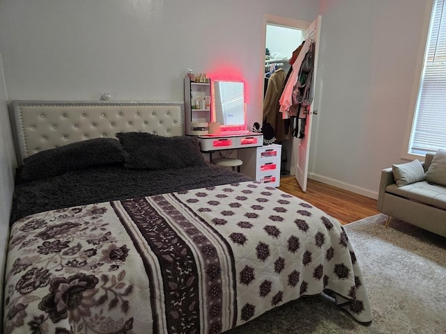 bedroom with wood finished floors, baseboards, a walk in closet, and a closet