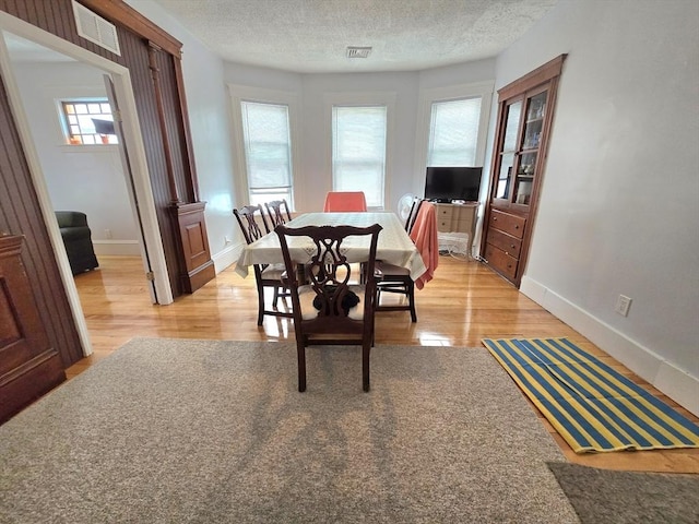 dining area featuring light wood-style flooring, baseboards, and a textured ceiling