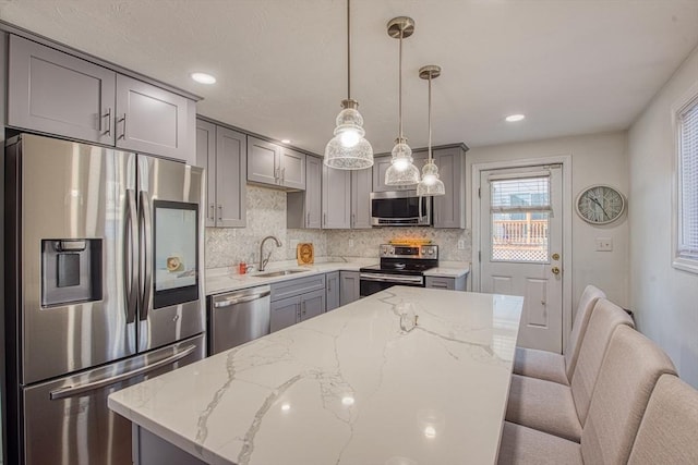 kitchen featuring light stone countertops, a sink, gray cabinetry, appliances with stainless steel finishes, and backsplash