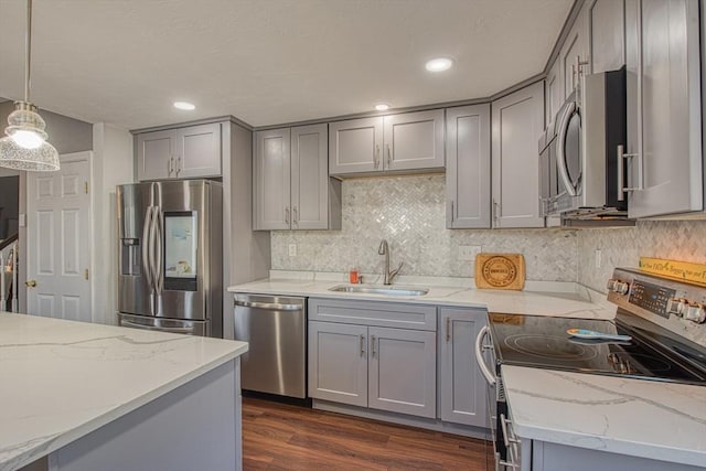 kitchen with gray cabinets, appliances with stainless steel finishes, light stone countertops, and a sink