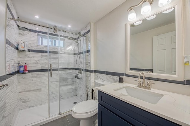 bathroom with a shower stall, toilet, vanity, tile patterned floors, and tile walls