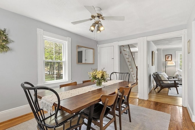 dining space with baseboards, light wood finished floors, a ceiling fan, and stairs