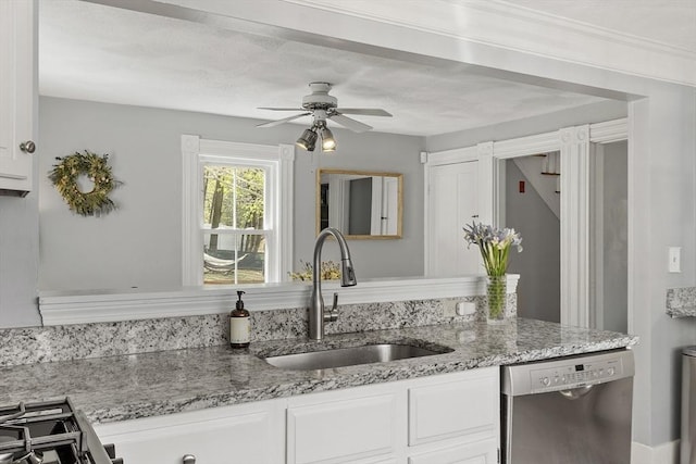 kitchen with a ceiling fan, stainless steel dishwasher, a sink, light stone counters, and white cabinetry