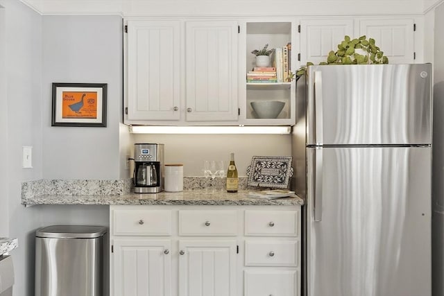 kitchen with light stone counters, freestanding refrigerator, and white cabinetry