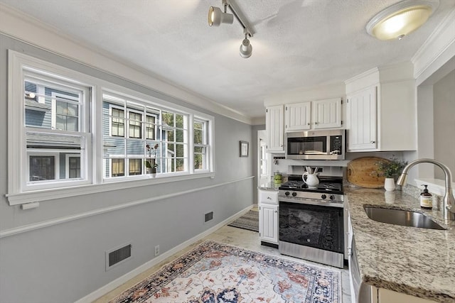 kitchen with white cabinets, light stone countertops, appliances with stainless steel finishes, a sink, and baseboards