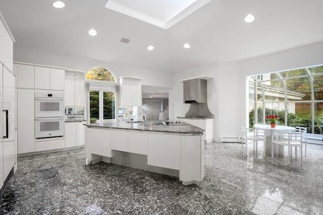 kitchen with a baseboard radiator, stainless steel microwave, white cabinetry, dark stone countertops, and double oven