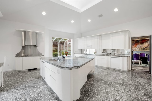 kitchen with sink, white cabinetry, dark stone counters, and an island with sink