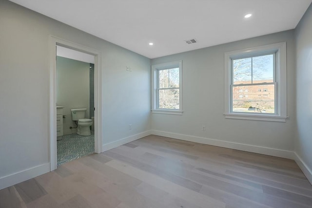 unfurnished bedroom with ensuite bath and light wood-type flooring