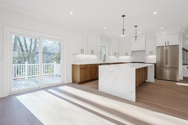 kitchen with decorative light fixtures, stainless steel fridge, a kitchen island, and white cabinetry