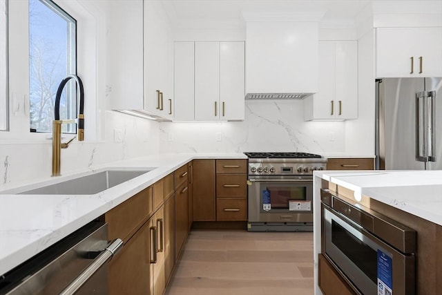 kitchen featuring white cabinetry, sink, light stone countertops, premium appliances, and light hardwood / wood-style flooring