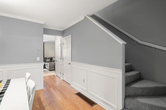 stairway with visible vents, wood finished floors, a wainscoted wall, ornamental molding, and a decorative wall