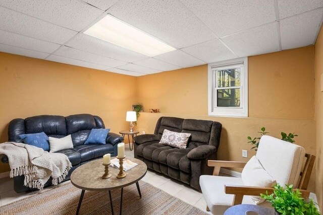living room featuring baseboards, light tile patterned floors, and a drop ceiling