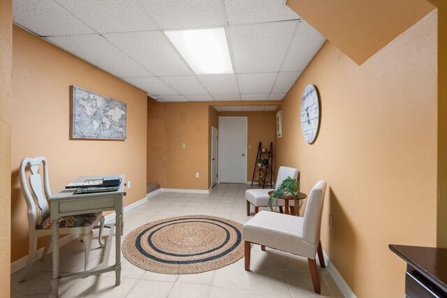 living area with baseboards, a drop ceiling, and light tile patterned floors