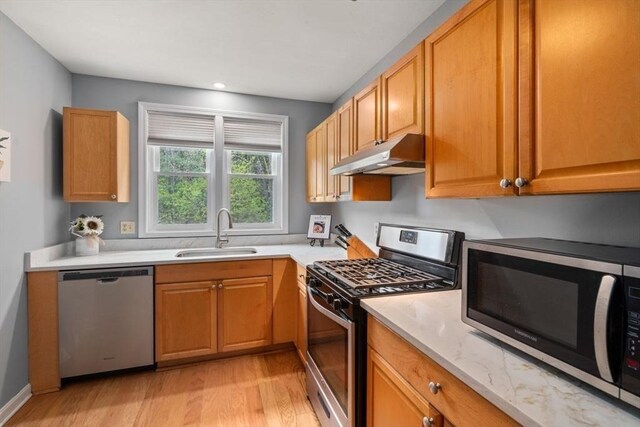 kitchen featuring a sink, light wood finished floors, appliances with stainless steel finishes, and under cabinet range hood