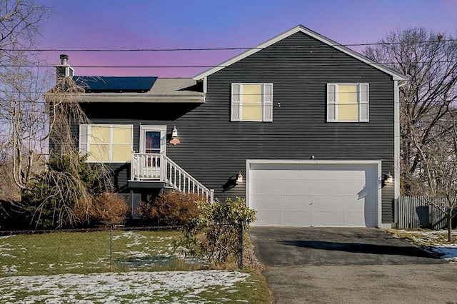 view of front of house with aphalt driveway, roof mounted solar panels, an attached garage, and fence