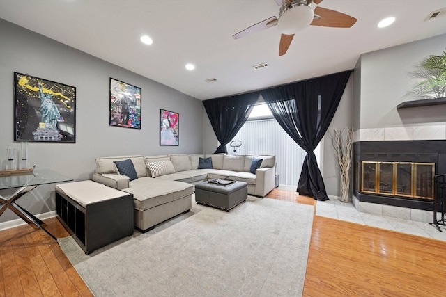 living room with hardwood / wood-style floors, a tiled fireplace, and ceiling fan