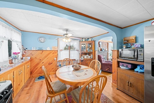 dining area with ornamental molding, arched walkways, light wood-type flooring, and ceiling fan