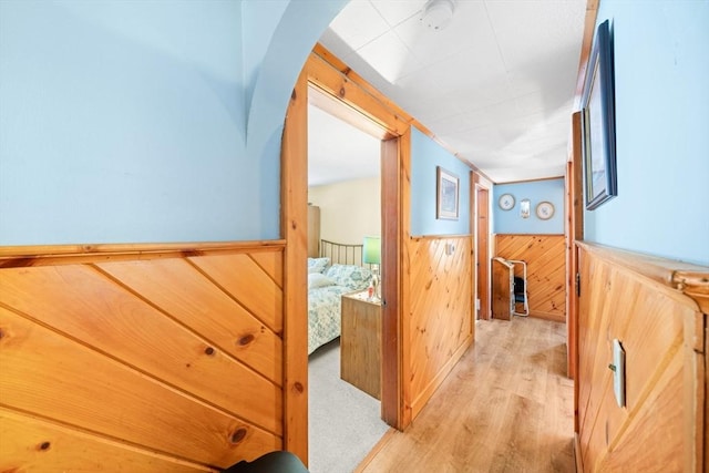 corridor with arched walkways, wainscoting, wood walls, and light wood-style flooring