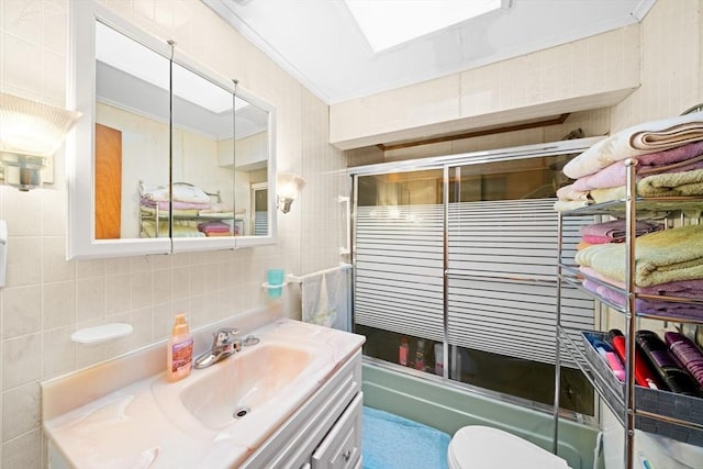 full bathroom with enclosed tub / shower combo, toilet, vanity, and tile walls