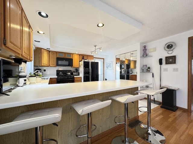 kitchen featuring black appliances, light hardwood / wood-style flooring, kitchen peninsula, and a breakfast bar