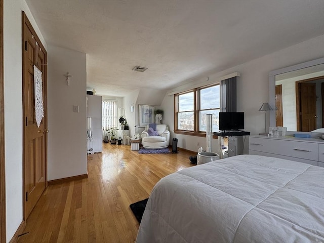 bedroom with light wood-type flooring, vaulted ceiling, and high end fridge