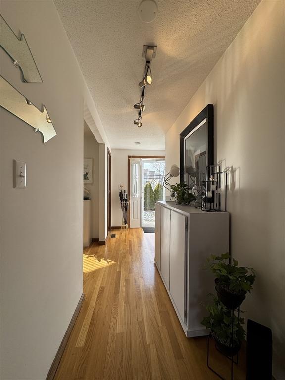 hallway featuring track lighting, light hardwood / wood-style floors, and a textured ceiling