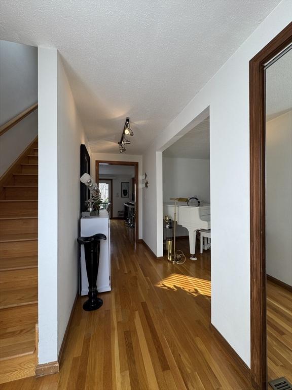 corridor featuring wood-type flooring, a textured ceiling, and track lighting