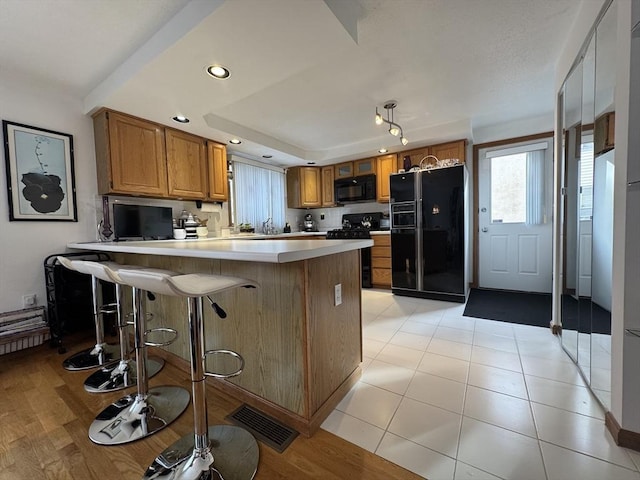 kitchen featuring black appliances, light tile patterned floors, a kitchen breakfast bar, a raised ceiling, and kitchen peninsula