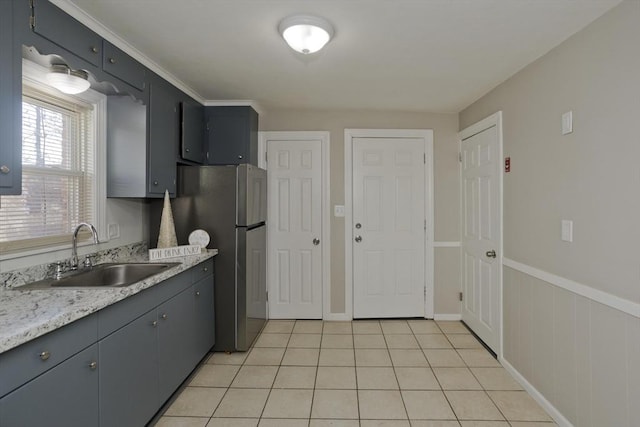 kitchen with light tile patterned flooring, stainless steel refrigerator, light stone countertops, and sink