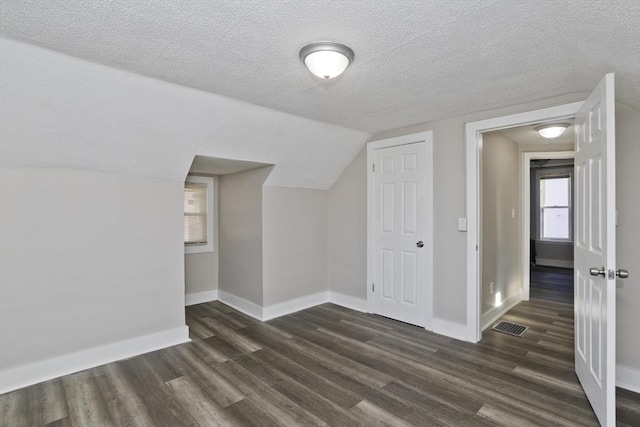 additional living space featuring a textured ceiling, dark hardwood / wood-style flooring, and lofted ceiling