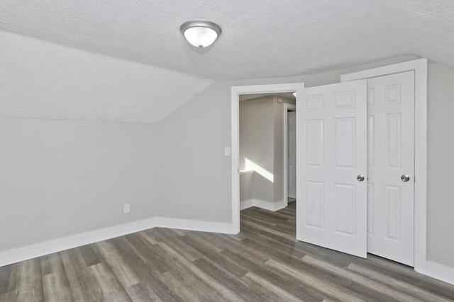 additional living space with a textured ceiling, dark hardwood / wood-style flooring, and lofted ceiling