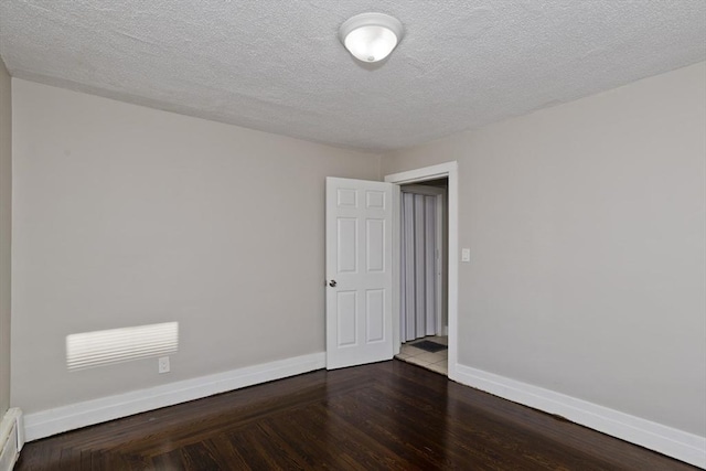 empty room with a textured ceiling and dark hardwood / wood-style floors