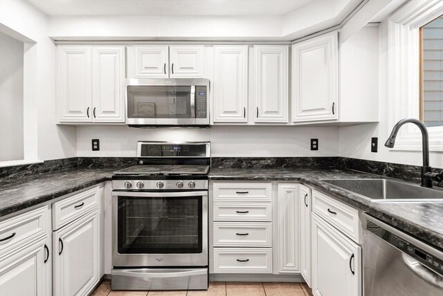 kitchen featuring appliances with stainless steel finishes, sink, white cabinets, dark stone counters, and light tile patterned floors