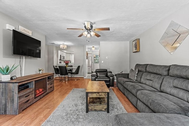 living room with ceiling fan, a textured ceiling, and light wood-type flooring