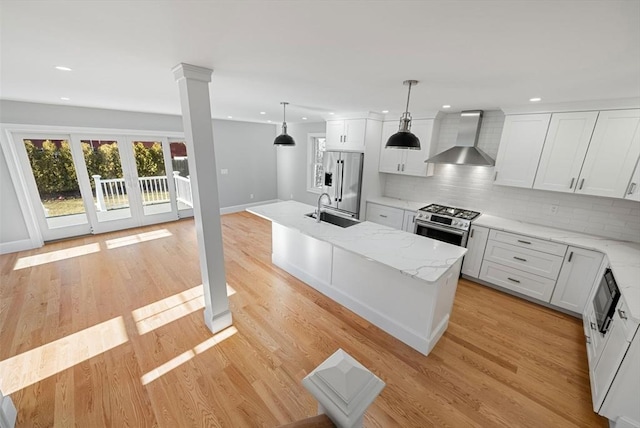 kitchen with appliances with stainless steel finishes, a center island, pendant lighting, white cabinets, and wall chimney range hood