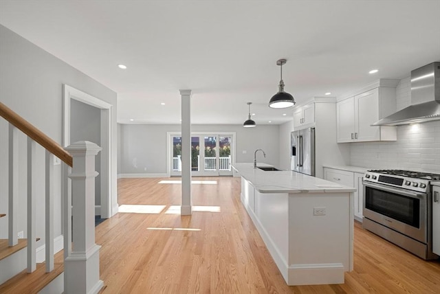 kitchen with a kitchen island with sink, appliances with stainless steel finishes, light stone counters, wall chimney exhaust hood, and white cabinetry