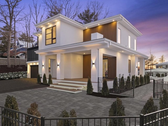 rear view of property with decorative driveway, stucco siding, covered porch, fence, and a garage